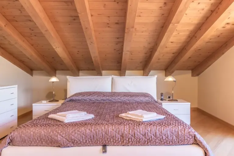 Camera matrimoniale mansardata di Apartment Tulipani 13 con soffitti in legno a vista e comodini illuminati