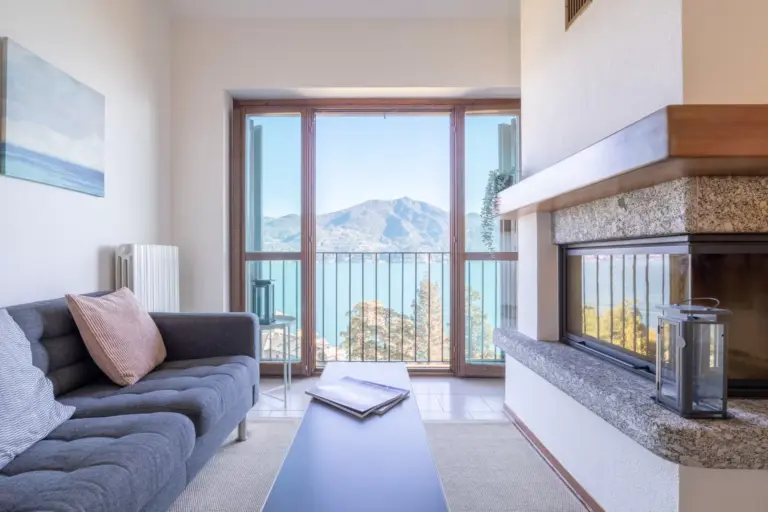 Soggiorno con divano e camino e finestra con vista lago dell'Appartamento Sole-Luce a Menaggio