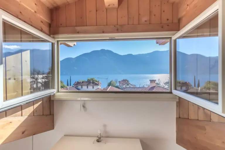 Finestra ad angolo a nastro che incornicia il Lago di Como e le montagne dalla mansarda dell'Apartment Tulipani 17