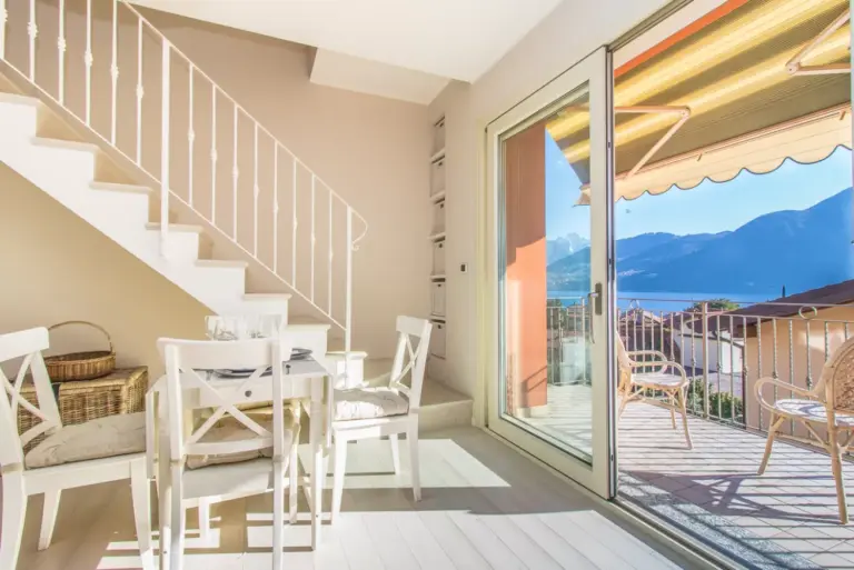 Zona pranzo con tavolo bianco, scala interna e portafinestra sulla terrazza vista lago dell'appartamento Tulipani 17